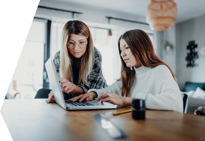 Eine junge Frau sitzt am Laptop. Ihre Mutter steht beratend neben ihr.